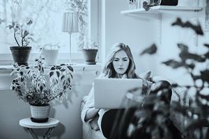 Woman on sofa with laptop surrounded by plants
