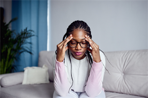 Woman sat on sofa with hands on her forehead