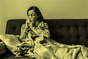 Person sat on a sofa under a blanket and blowing their nose