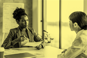 Two people sat at a desk talking