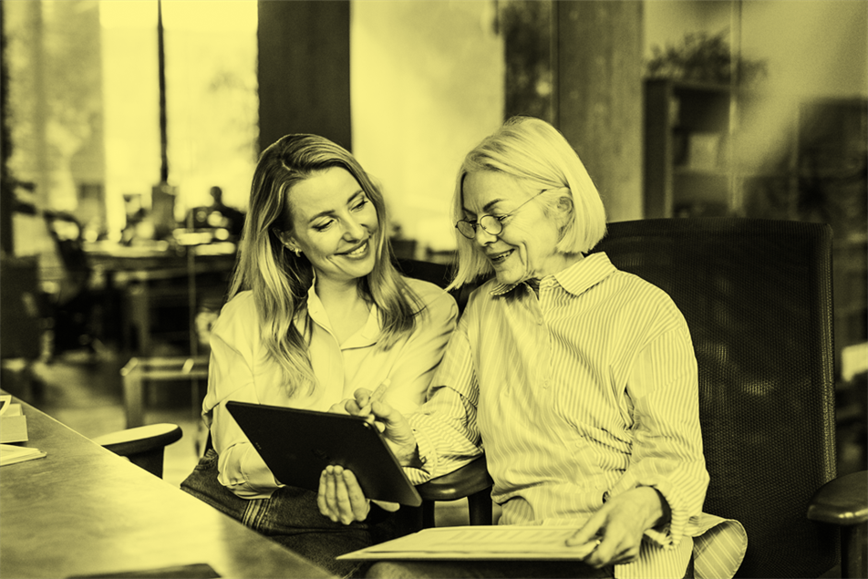 Two people sat at a desk holding a tablet